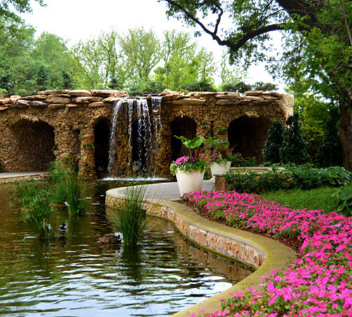 the Arboretum's flowers beside a pond with waterfall and trees in background
