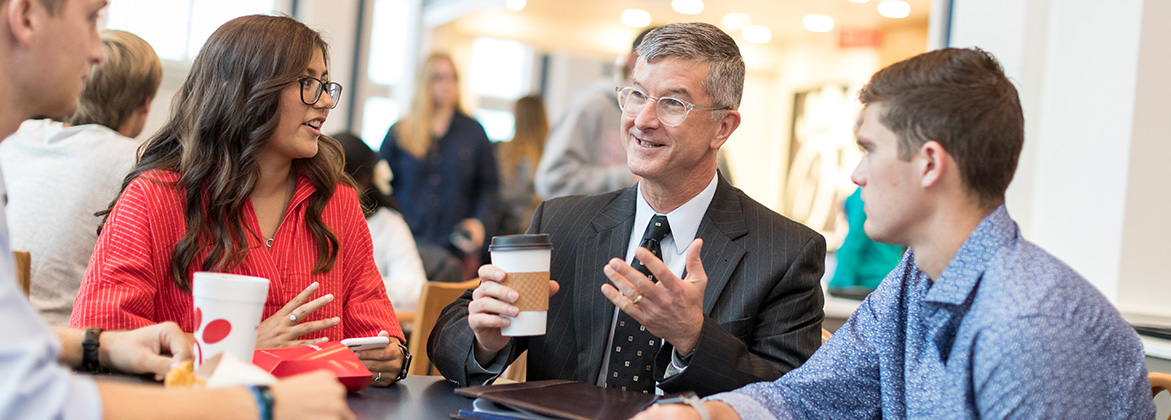 professors talks with group of students over coffee