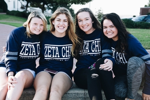 Four girls posing together wearing Zeta Chi blue sweatshirts outside