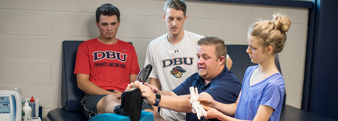 athletic trainer working with athlete while interns watch