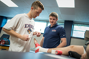 male student learning how to wrap a foot with trainer professor supervising