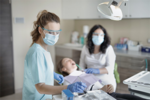 women in blue scrubs working on patient in dentist chair