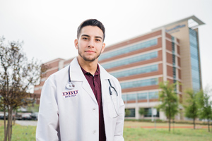 picture of a student with a DBU white coat in front of a hospital