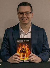 Christian Englert smiles in a blue blazer, holding his book "Refined by Fire" with a flame cover