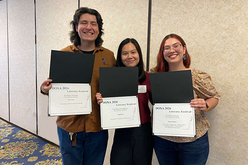 three college students standing indoors holding an award