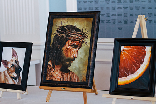 Painting of Jesus wearing a crown of thorns displayed on an easel with other framed paintings nearby