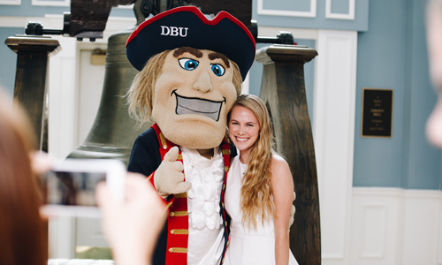 girl taking a picture with DBU mascot by the bell in mahler student center