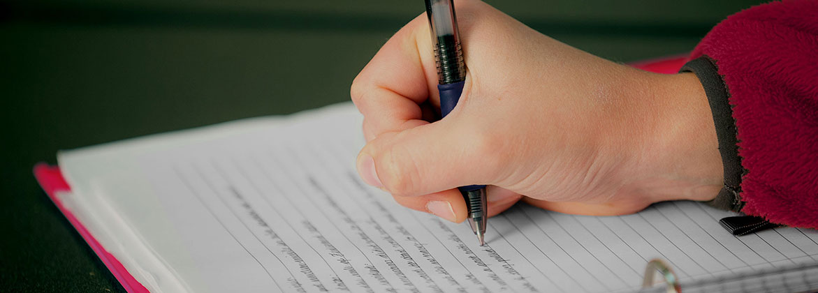 A student writing on a paper with a pen. 