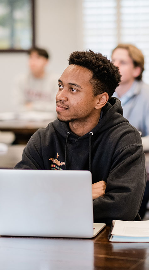 college student sitting in class looking at teacher with laptop