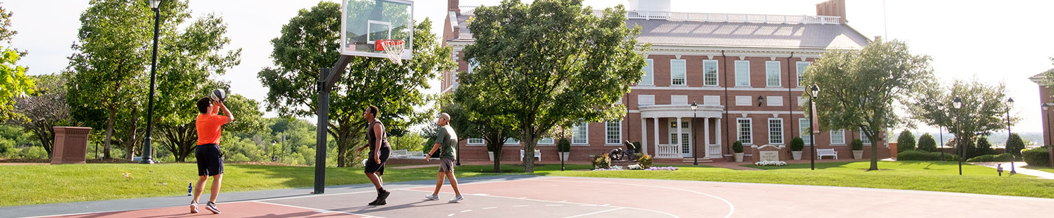 Wide campus beauty photo of DBU architecture with students playing basketball