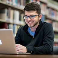 picture of a man wearing glasses smiling at his computer in the library