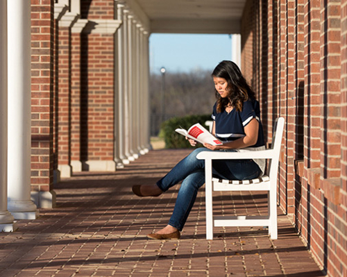 student sitting outside on a bench reading a book outside of the coffeeshop and the union grill