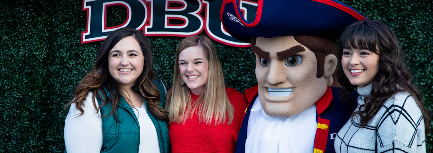 three women stand smiling with the patriot mascot