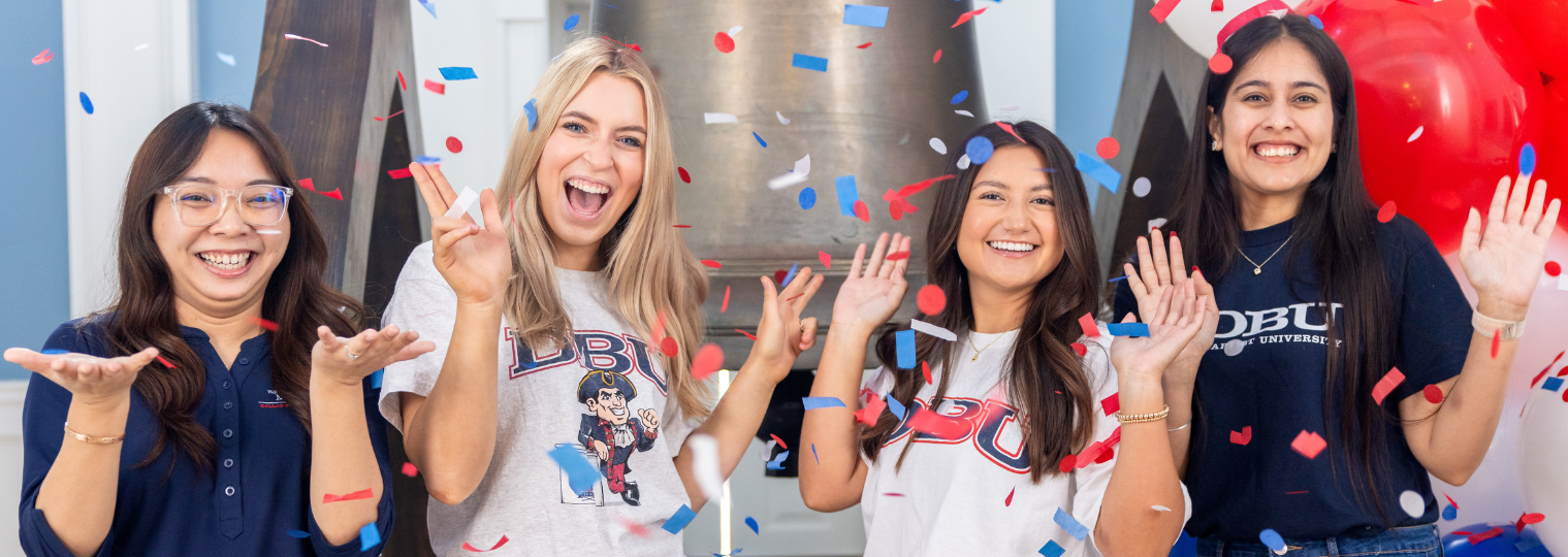 three women stand smiling with the patriot mascot