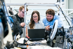 three individuals smiling and looking at the computer inside of a car