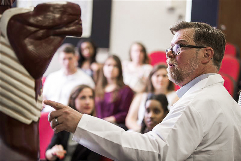 A professor teaches in front of an anatomy model to a class full of students