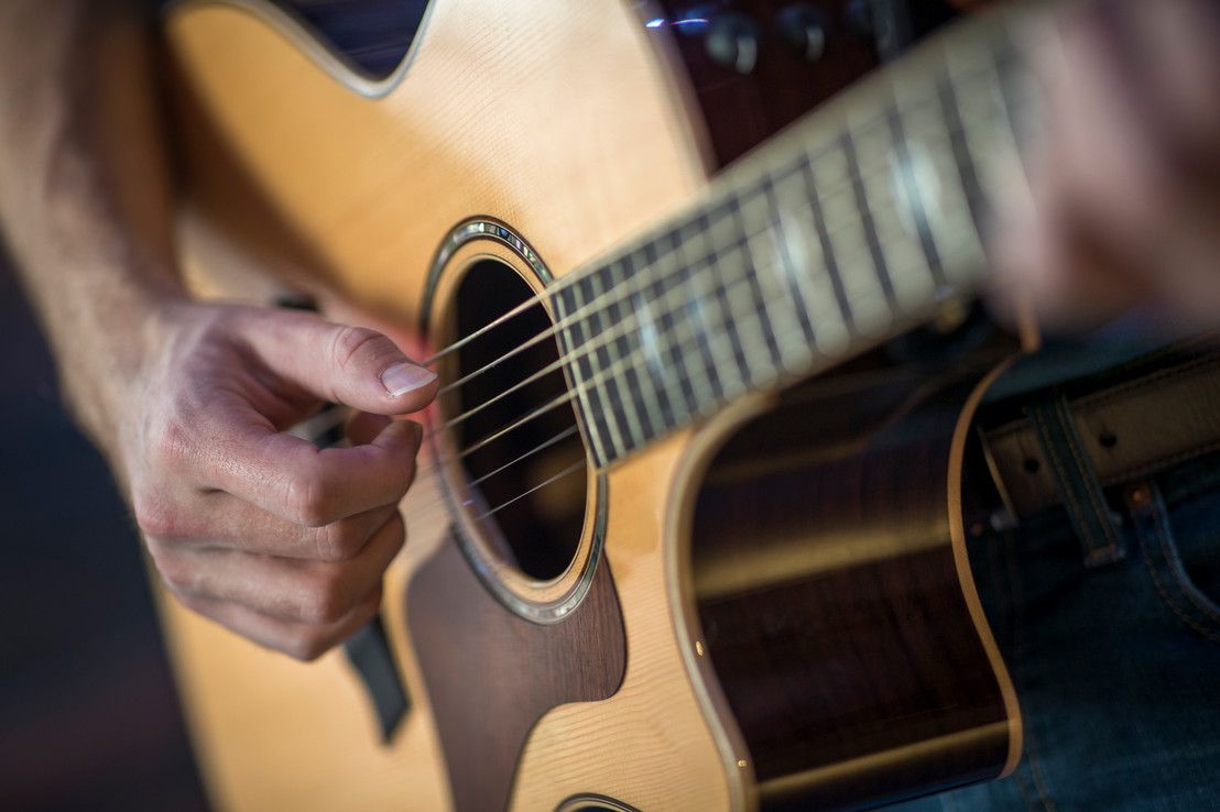 a close up of a man playing a tan acoustic guitar in Dallas, Texas