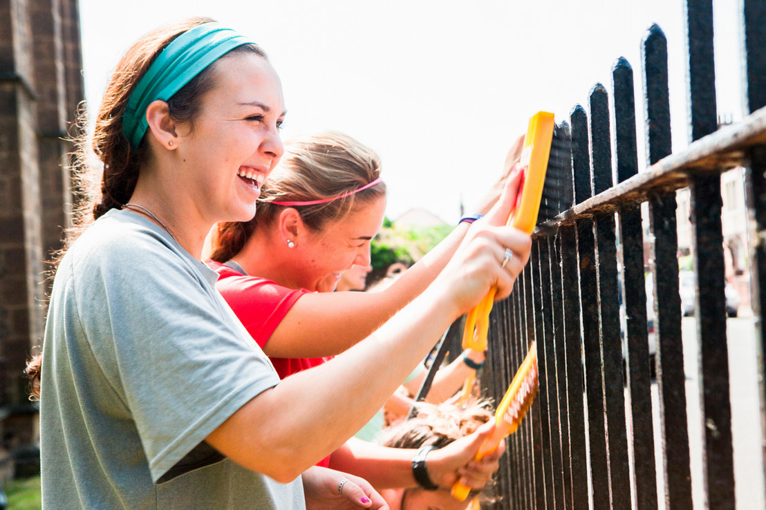college students in Dallas, Texas smiling as they clean a metal fence together for a service project