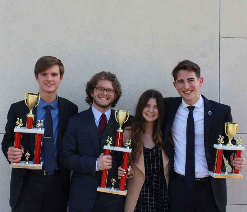 Four debaters holding trophies