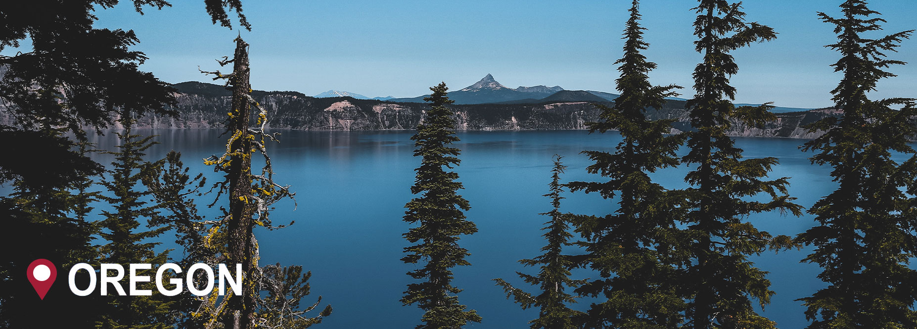 A lake with tall pine and spruce trees surrounding it with mountains in the distance