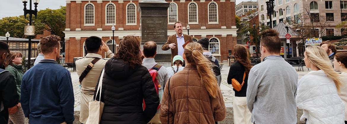 A professor lectures in a Boston square in front of a statue