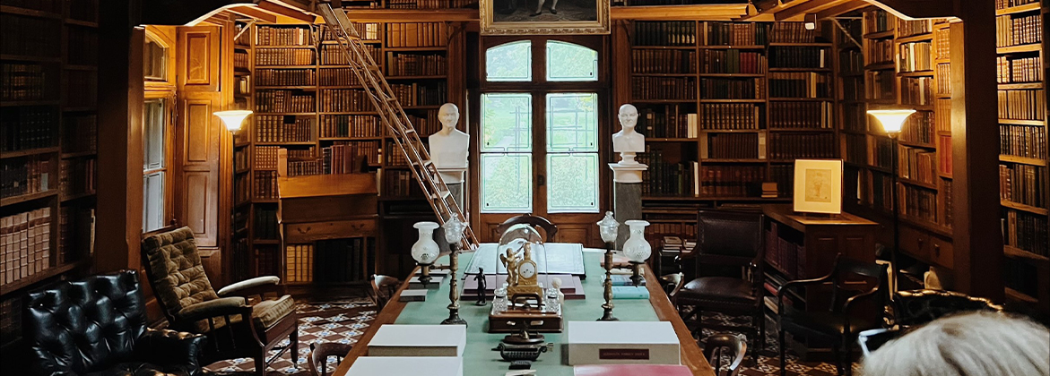 Library alcove filled floor to ceiling with books and sculpture, with two historical portraits hanging from the balcony railing