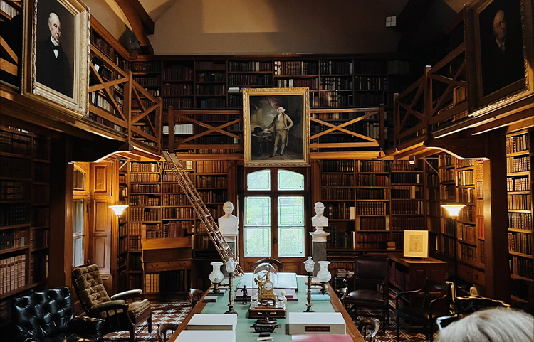 Small library alcove filled to the ceiling with books with two historical portraits hanging on balcony