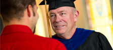 older gentleman wearing graduation cap talking with younger guy wearing a red shirt