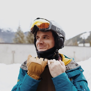 1. Picture of a guy in ski gear looking off to the distance who is wearing a blue jacket and yellow-reflective ski goggles