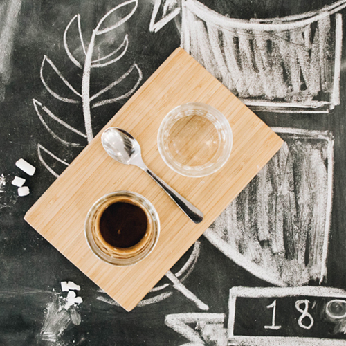 A wooden block with a spoon and two glass cups resting on it. In the background there are chalk drawings