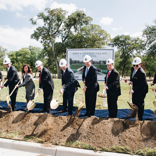 A group of people in suits posing with hard hats on and shovels alongside a pile of dirt for the Ford Village ground breaking