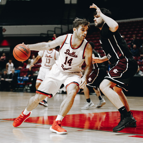 A basketball player (number 14) dribbling around another player on the court