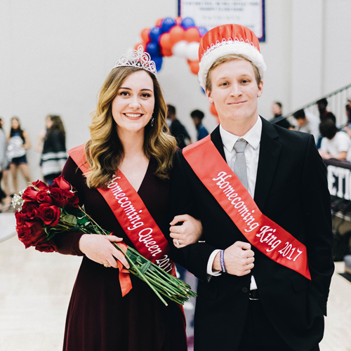 The homecoming queen and king, with red sashes on and a bouquet of red roses