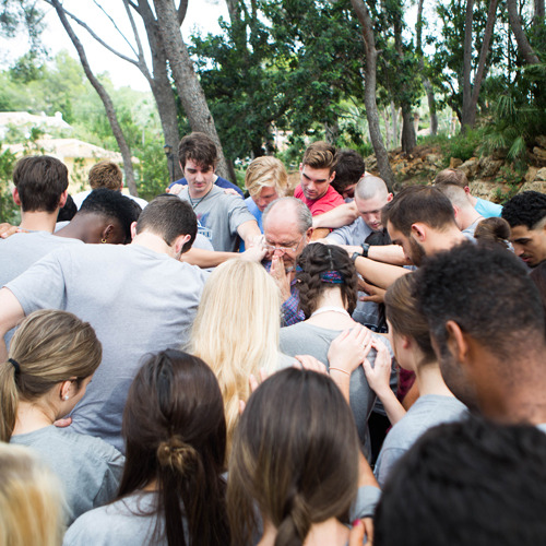 A group of people praying, all of their heads are bowed, and they are all outside