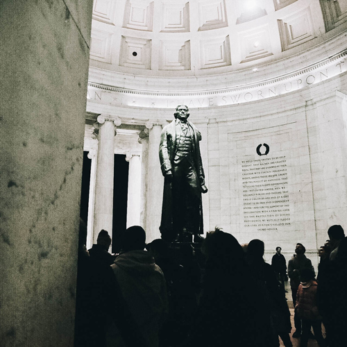 A statue of Thomas Jefferson inside the memorial building with people surrounding it.