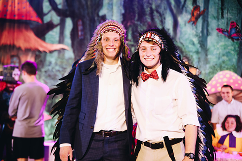 Two guys posing together at Mr. Big Chief, both are wearing headdresses. The one on the right is wearing a red bowtie.