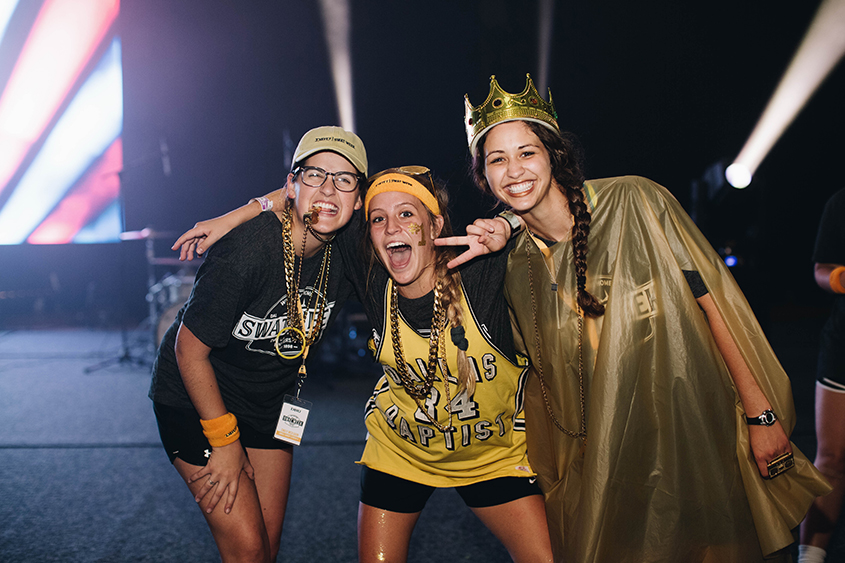 Three girls posing together wearing yellow and black, the girl on the far right is wearing a gold crown and the one in the middle is wearing a yellow jersey
