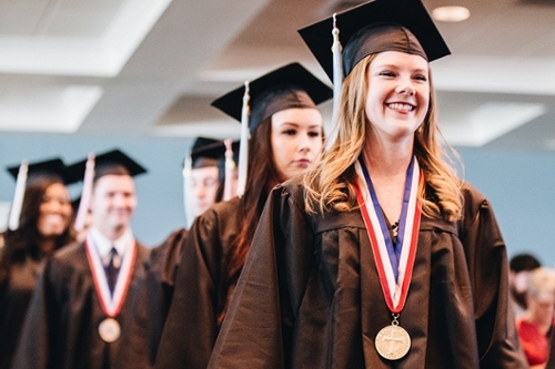 A line of DBU graduates, wearing caps and gowns and the leading girl is wearing a medallion