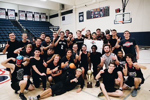 Group of guys wearing all black posing on the basketball court with a trophy on the floor