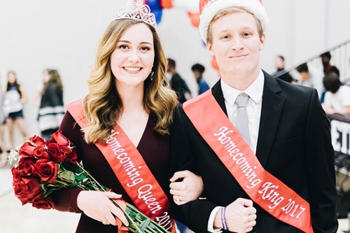 DBU Homecoming queen and king, the sash says 2017, they are both wearing crowns and the girl is holding a bouquet of red roses