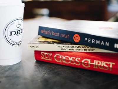 Books stacked on a table next to DBU Coffeehouse coffee