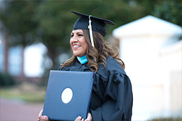 DBU grad poses with diploma after commencement outside the DBU chapel.