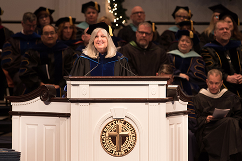 Dr. Joan Davis speaking at commencement service with faculty sitting behind her