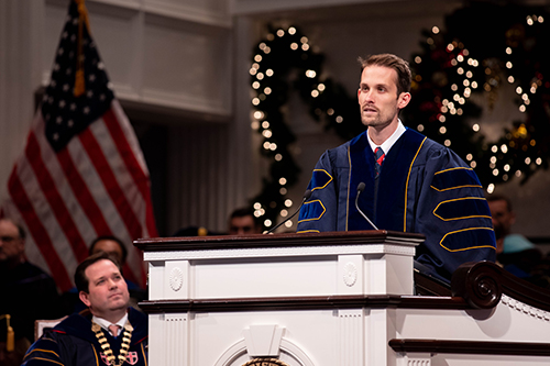 Mark Cook speaking during service - behind him is faculty member, American flag, and Christmas decor