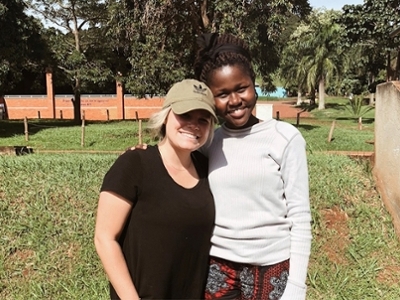 A female DBU Student is standing next to a girl from Uganda in Uganda. 