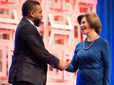 An African American is shaking hands with Barbara Bush on a stage.