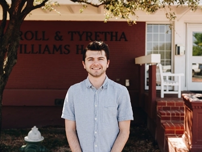 A male student is standing in front of Williams dorm. 