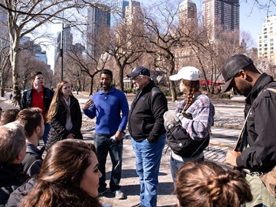 A group of students listen to a lecture in the middle of New York City. 