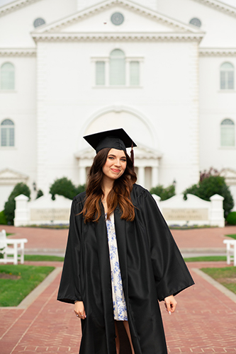 Ashley Huff standing in front of the DBU chapel wearing her graduation cap and gown