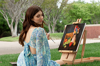 Ashley Huff sitting on a green field in Dallas, Texas painting